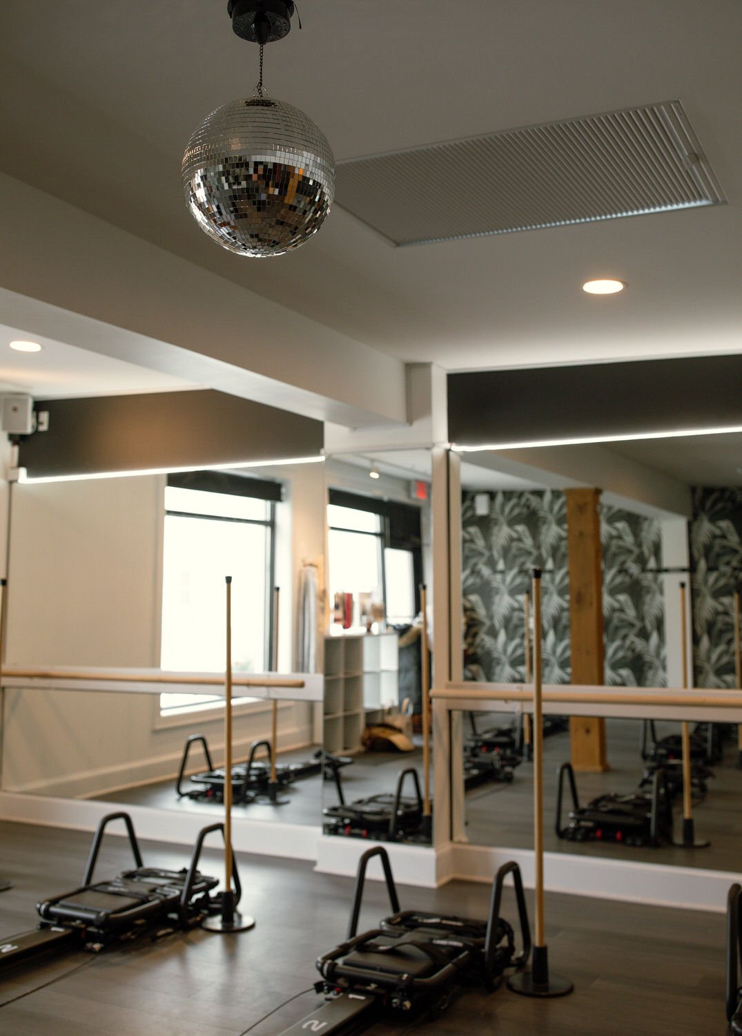 Interior of Lava Fitness with pilates reformer machines, a large mirror, a ceiling disco ball, and botanical wallpaper.