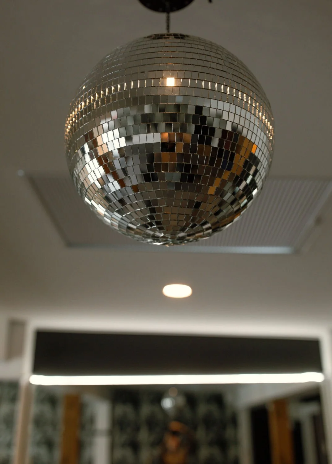 A large disco ball hanging from the ceiling in a room, reflecting light and surroundings.