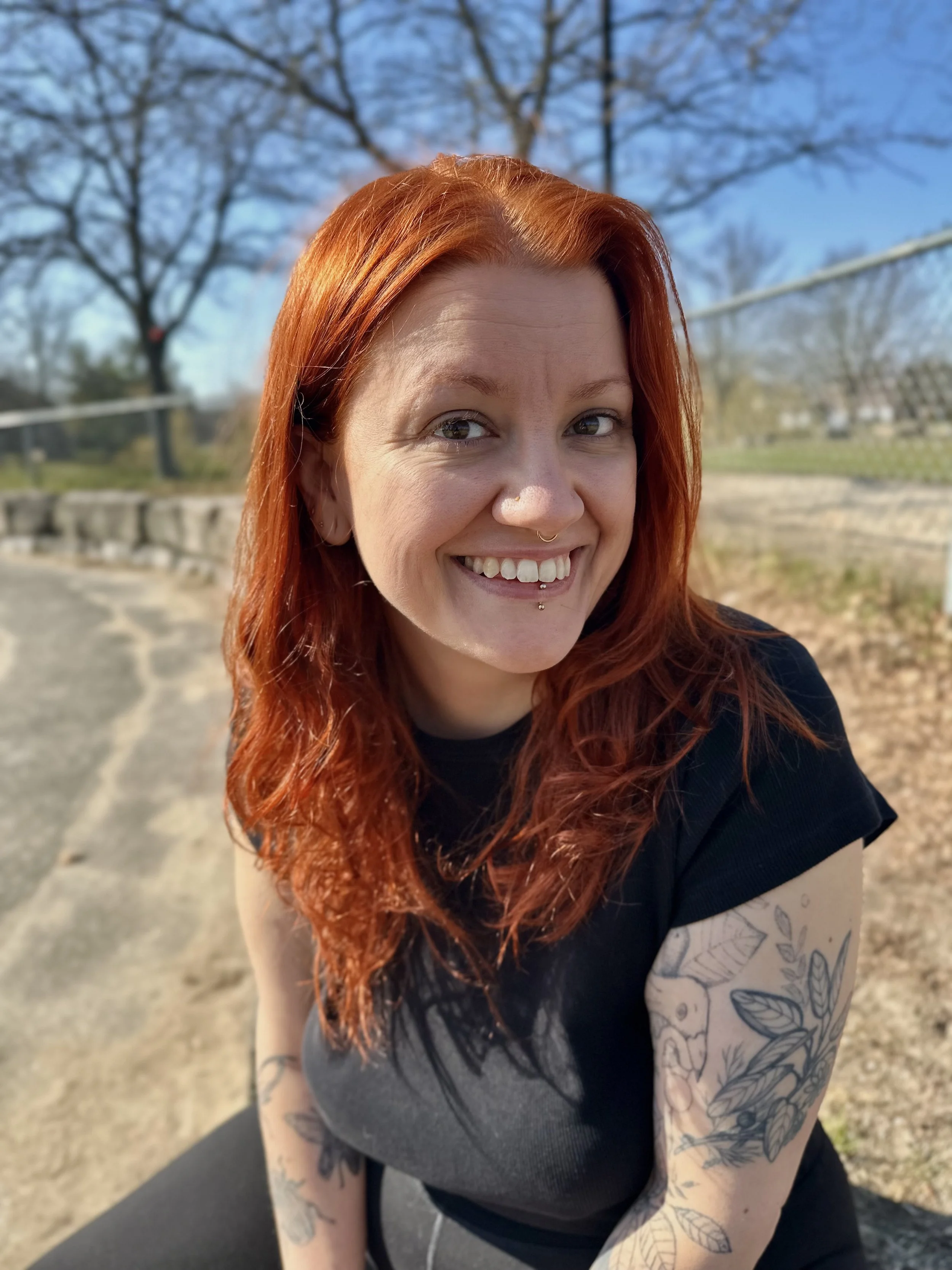 An image of Maeve Canning of Winter Creature Illustrations smiling with bright read hair and a black shirt.