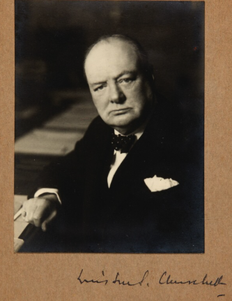 Black and white portrait of a serious man in a suit with a bow tie, sitting at a piano, signature at the bottom reading Louis Armstrong.