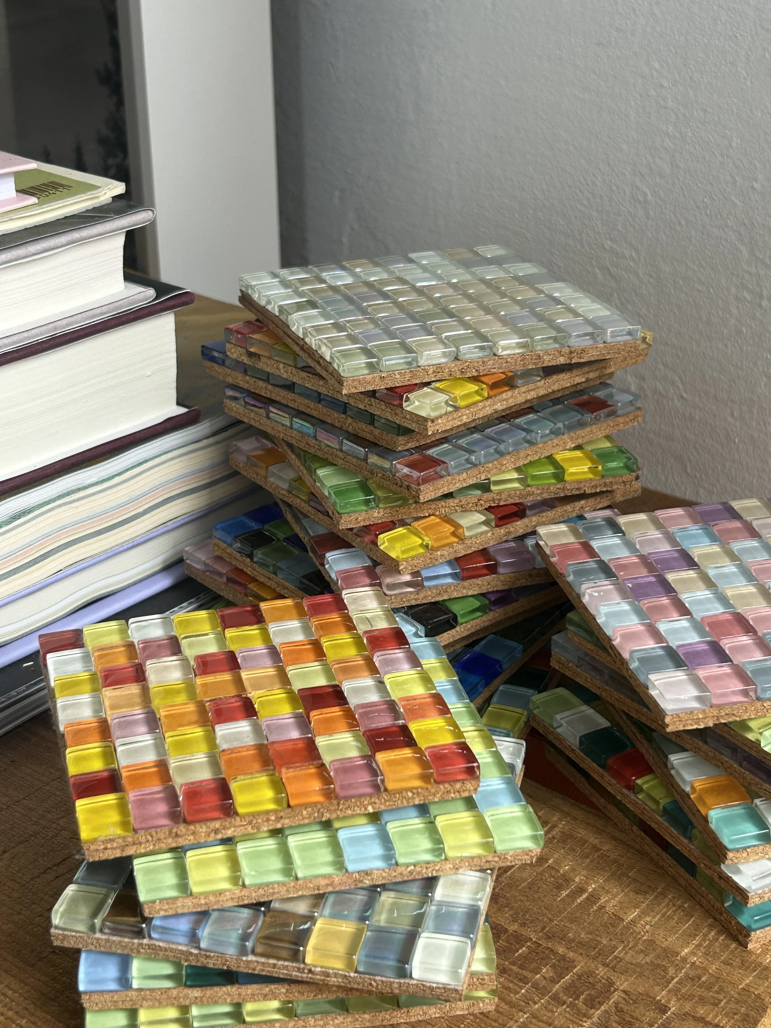 Stacked wooden coasters, on a wooden surface next to a pile of books.