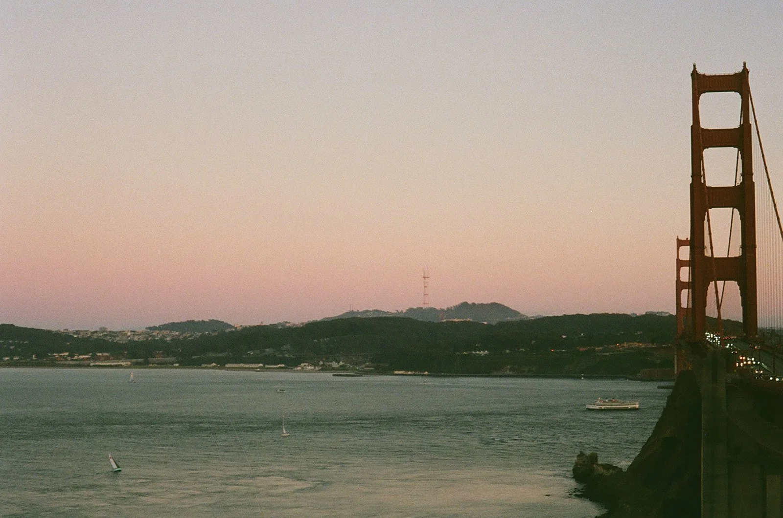 Golden Gate Bridge in San Francisco during sunset with sailboats on the water and hills in the background.