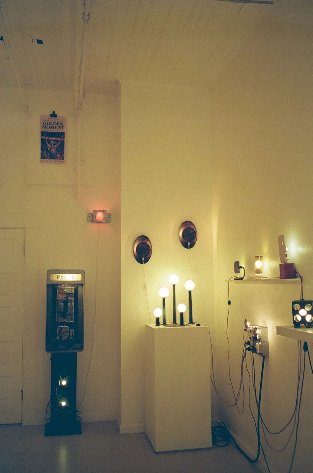 A display of various modern lamps and light fixtures in a gallery setting, with some sitting on pedestals and others mounted on the wall.