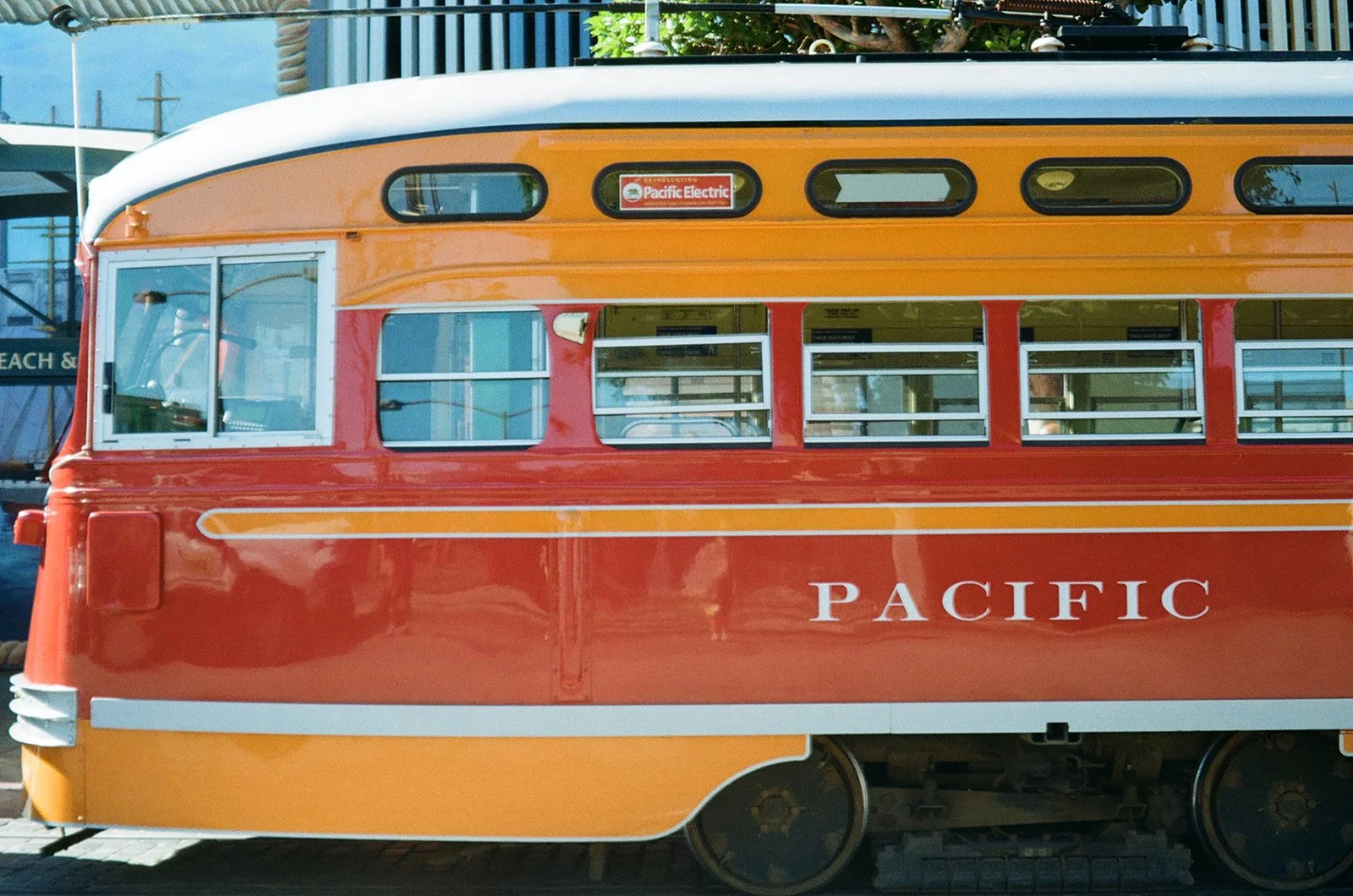 Colorful vintage trolley with orange, yellow, and red paint, marked 'Pacific Electric' and 'Pacific' on its side, in an outdoor setting.
