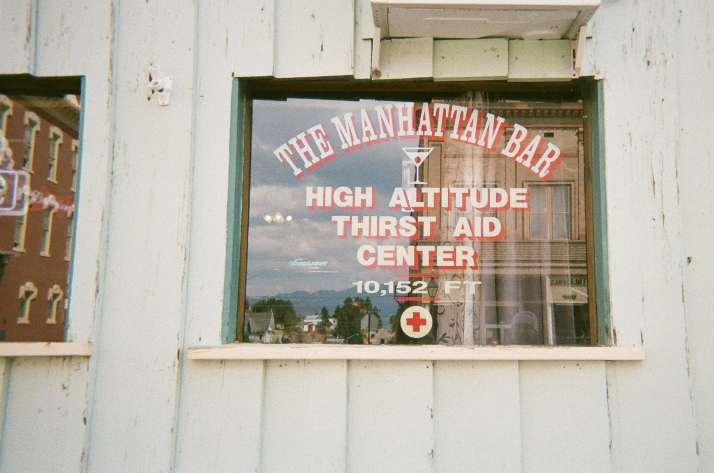 Sign on a window advertising 'The Manhattan Bar,' which is a high altitude thirst aid center at 10,152 feet.