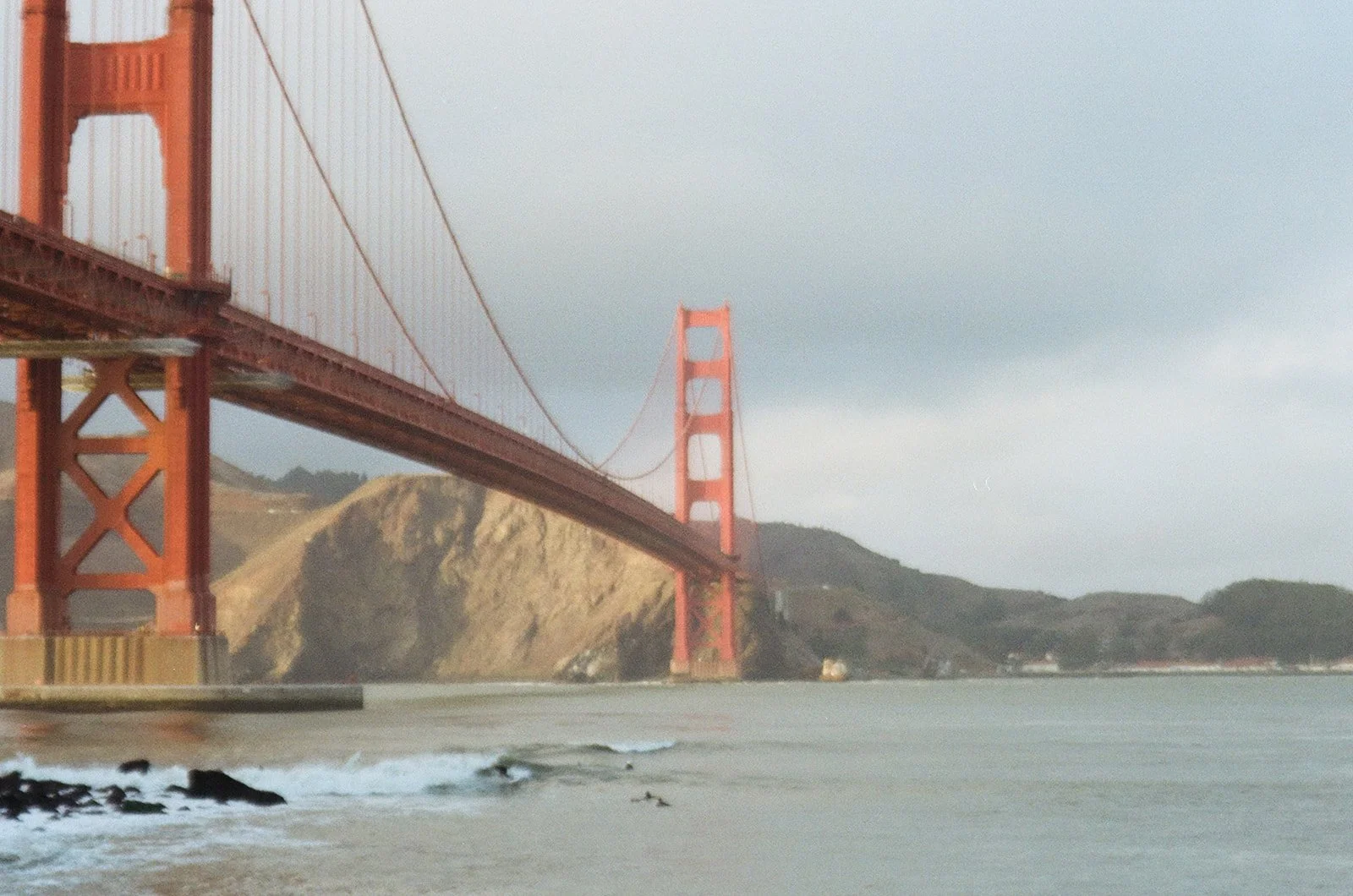 The Golden Gate Bridge in San Francisco, California, spanning over the water with hills in the background on a cloudy day.