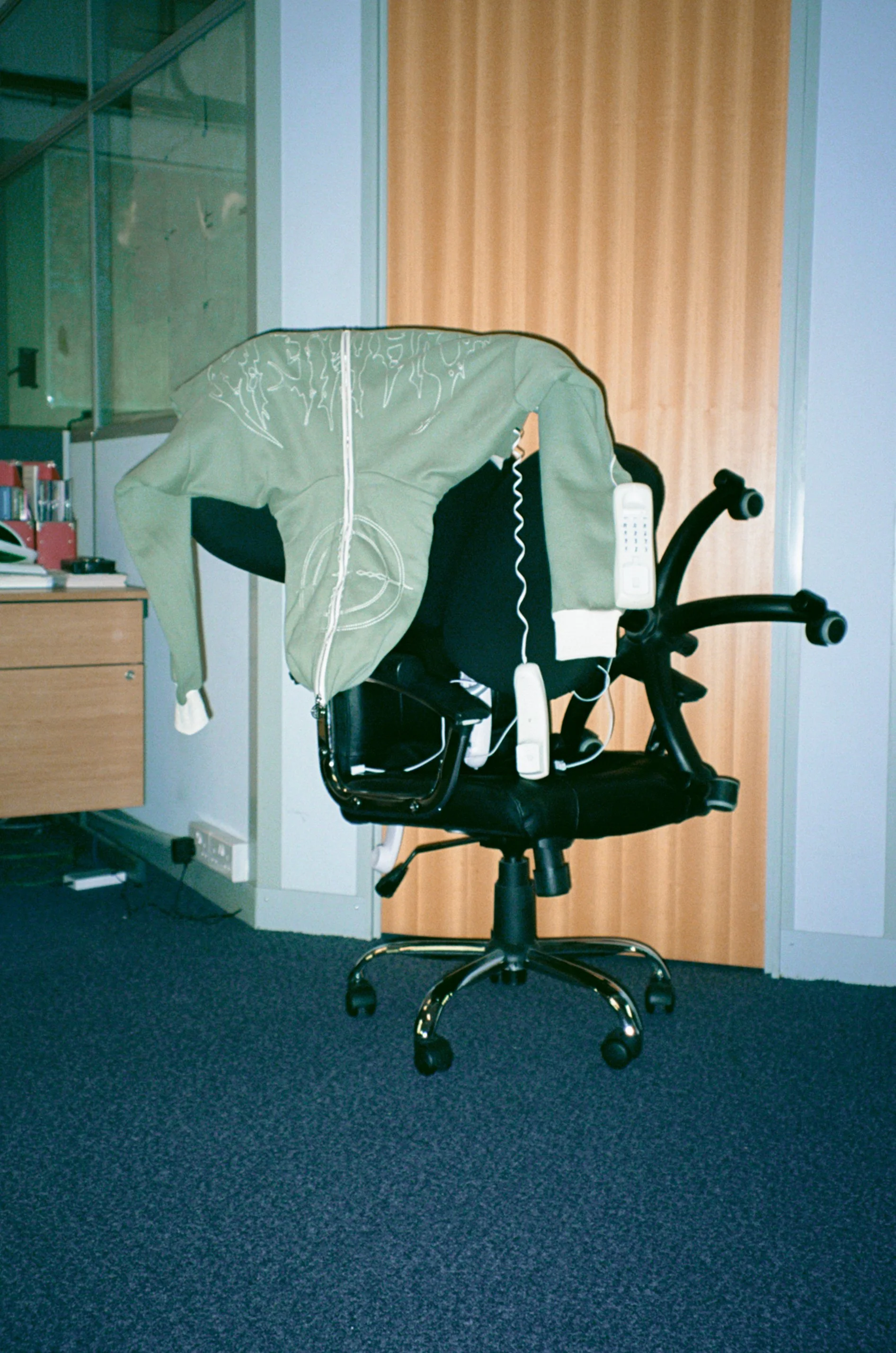 Launch campaign product image for NAMED Collective “Classified” featuring a green zip hoodie suspended on an office chair.