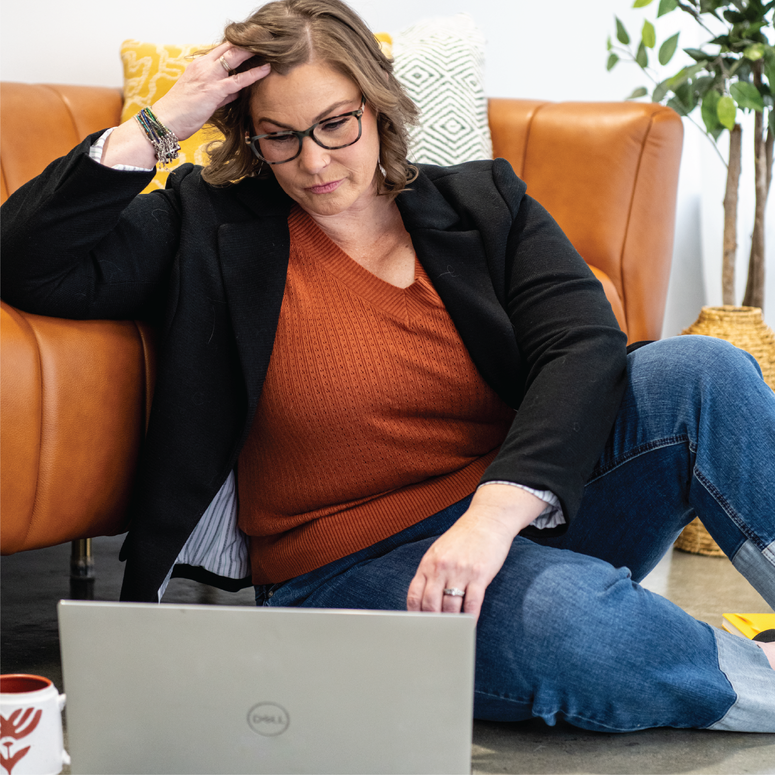 Woman sitting on the floor with a laptop, looking at the screen with a worried expression, touching her head.
