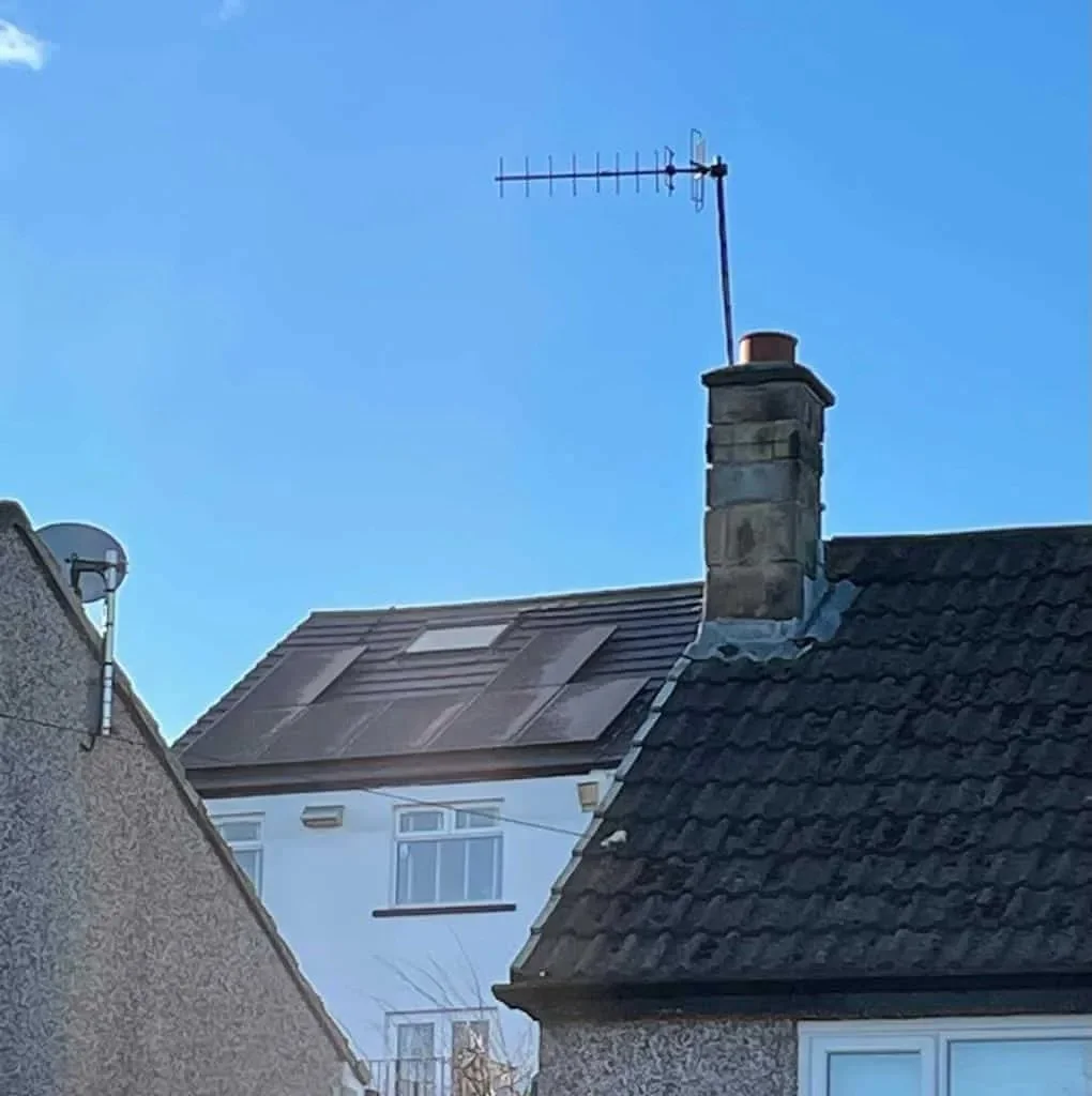 Residential rooftop solar panel installation on a white house, featuring black solar panels fitted around a roof window to maximise available roof space and renewable energy generation.