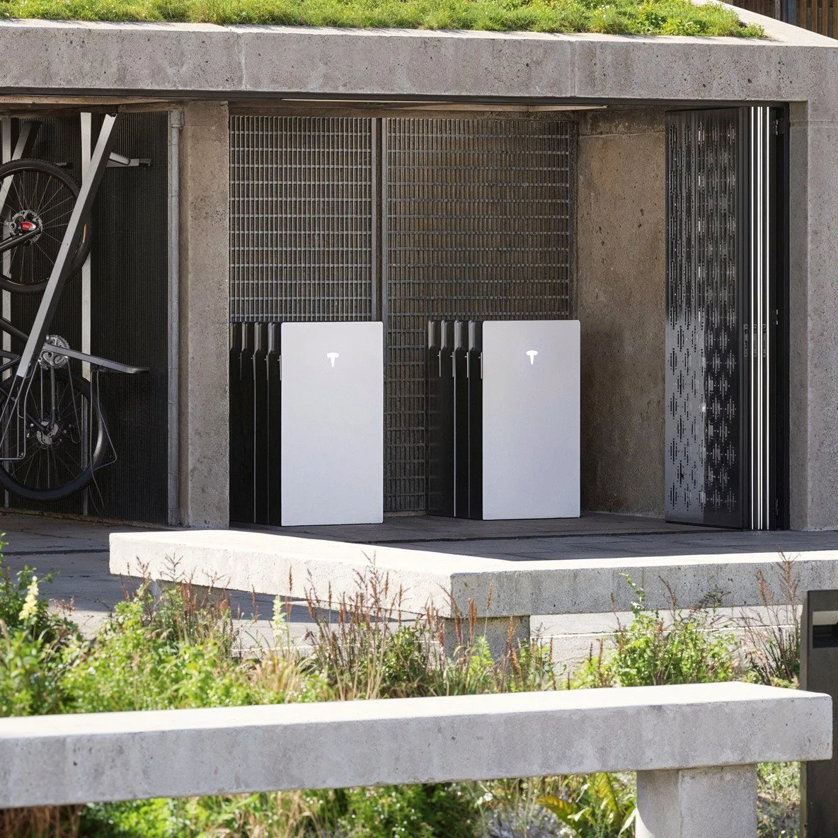 A modern bike storage area containing two bicycles and several Tesla charging units outside a building.