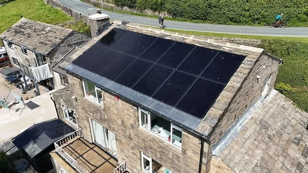Aerial view of solar panels installed on a flat roof surrounded by stone buildings, Keighley area