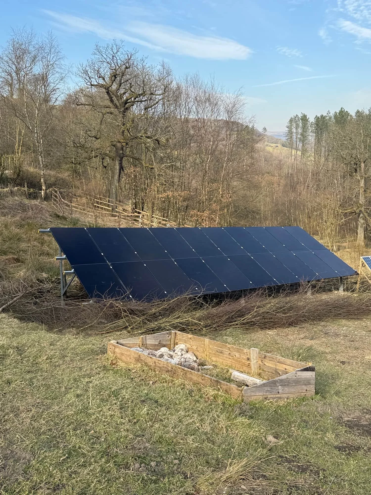 A solar panel installation on a grassy field with trees and a blue sky in the background.