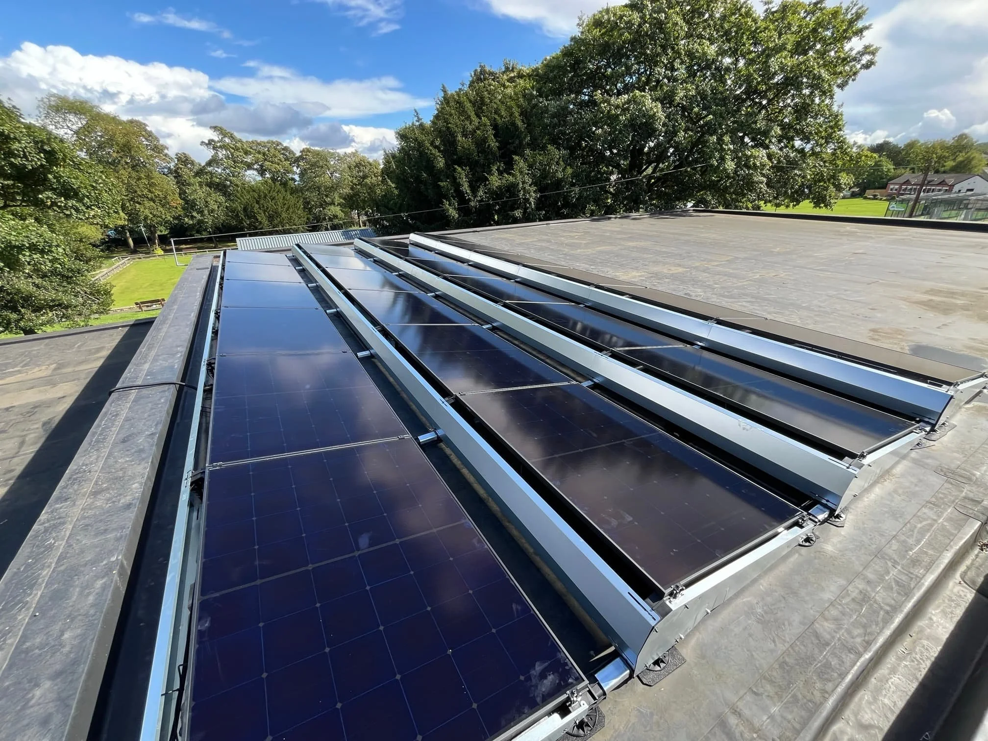 Solar panels installed on a flat rooftop with trees and a blue sky with some clouds in the background.