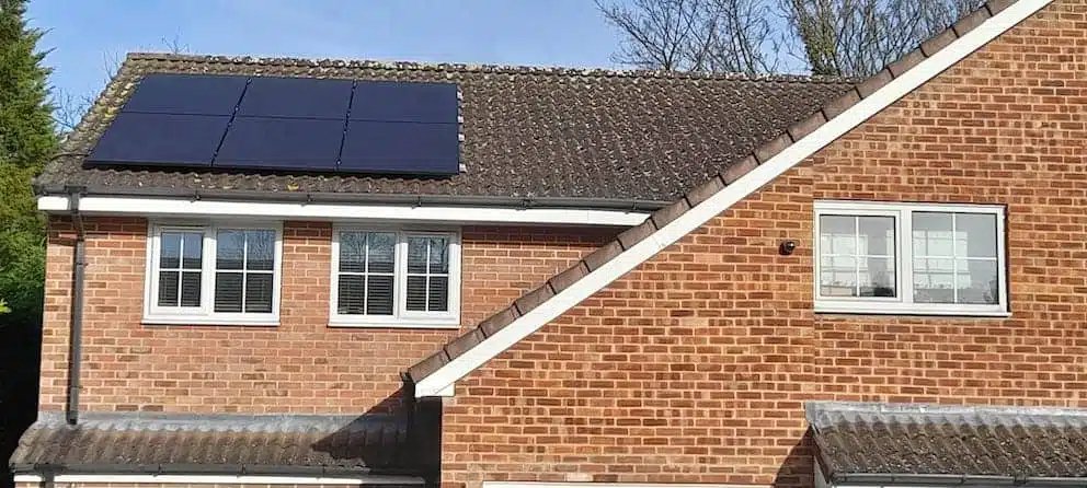 Residential brick home with a rooftop solar panel installation featuring six black solar panels mounted on a tiled roof, generating renewable energy and helping reduce household electricity costs.