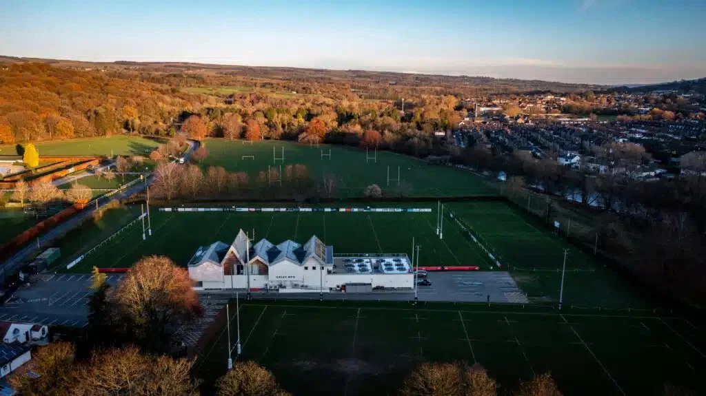Aerial view of Ilkley RFU clubhouse and rugby grounds showing the completed solar panel installation integrated into the building's distinctive roof design.