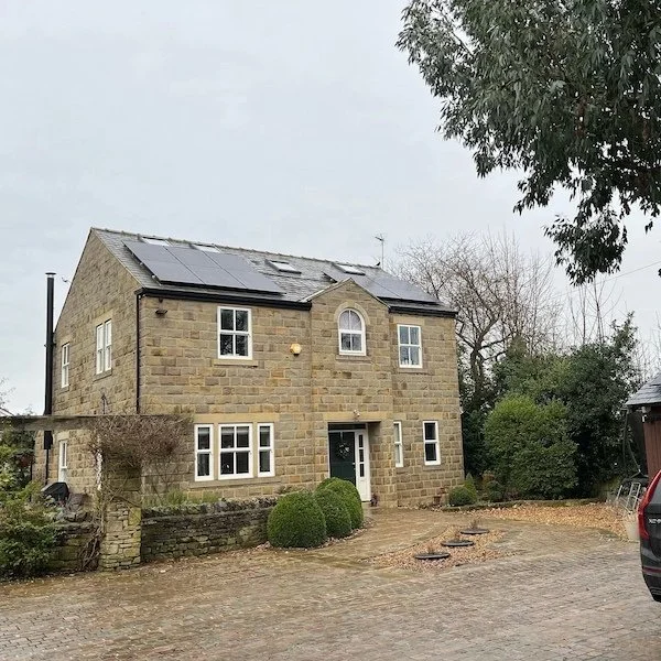 Stone-built detached house with solar panels installed on the roof, surrounded by trees, Ilkley