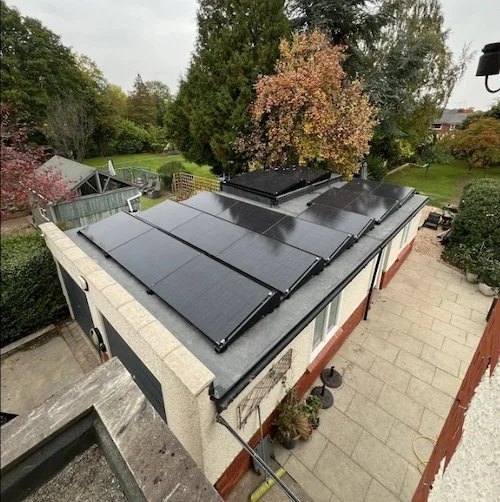 Aerial view of solar panels installed on a garage roof surrounded by garden trees