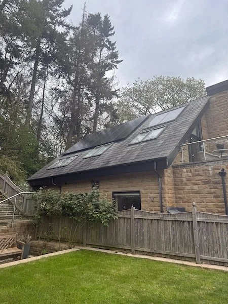 Solar panels installed on the roof of a stone property, viewed from the garden, Ilkley