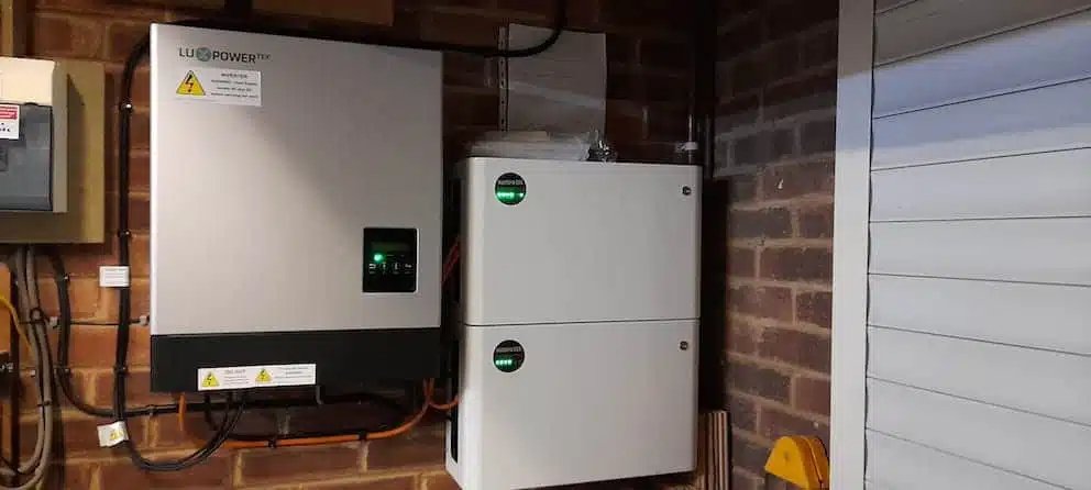 Wall-mounted solar inverter and battery storage system installed in a brick garage, designed to store excess solar energy, increase self-consumption, and reduce household reliance on grid electricity.