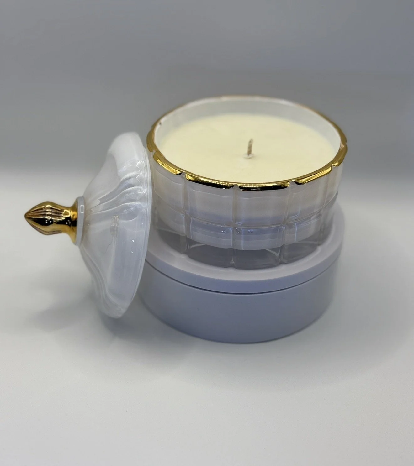 A decorative white candle in a glass container with gold accents, placed on a grey and white surface.