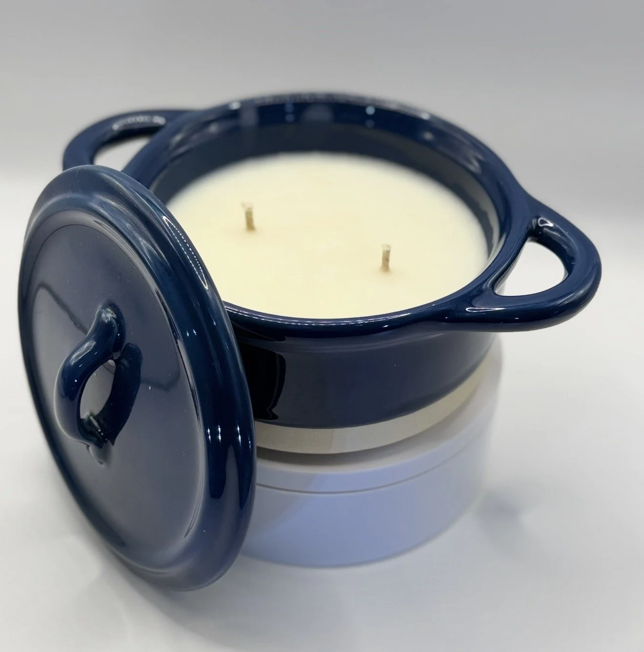 A dark blue ceramic pot with a matching lid, filled with white wax and two unlit candles.