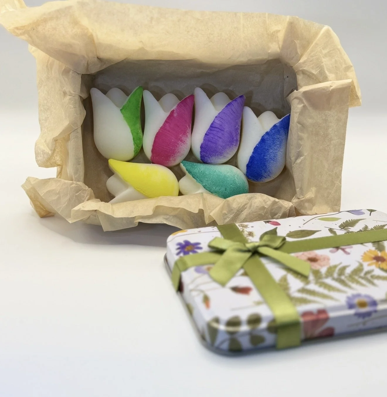 Colorful marshmallow candies shaped like flowers inside a paper-lined box with a floral gift box nearby.