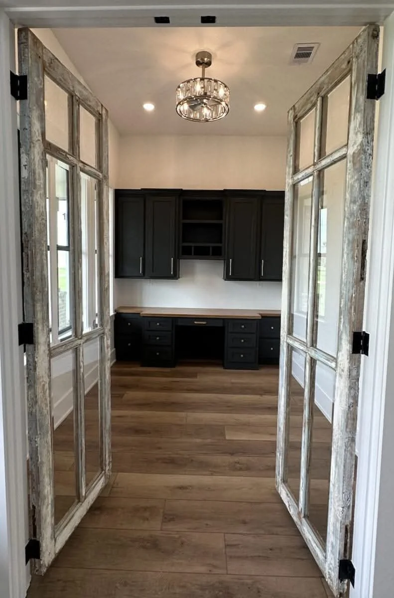 Viewing a home office with black cabinetry, a wood desk, and decorative rustic double doors.
