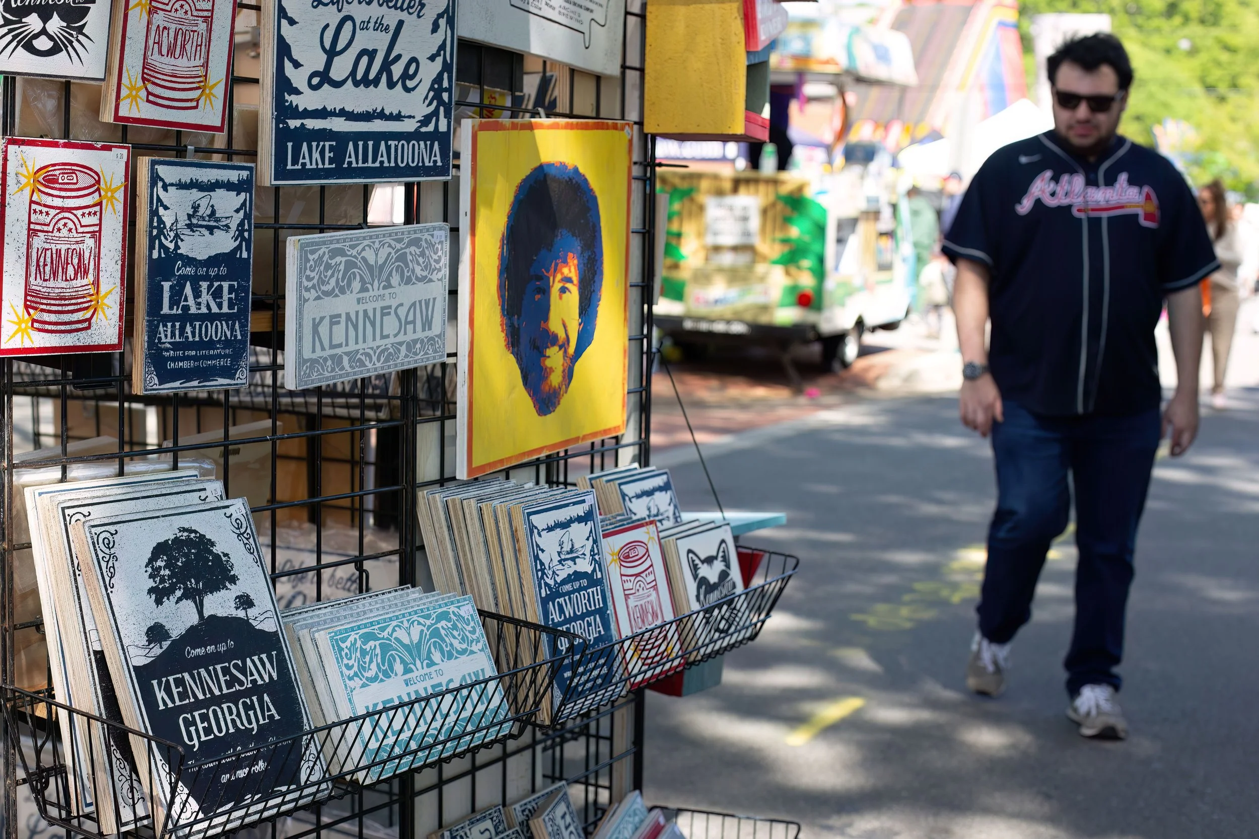 A display of souvenirs featuring signs and artwork promoting Lake Allatoona, Kennesaw, Georgia, and a colorful portrait of a man with an afro.