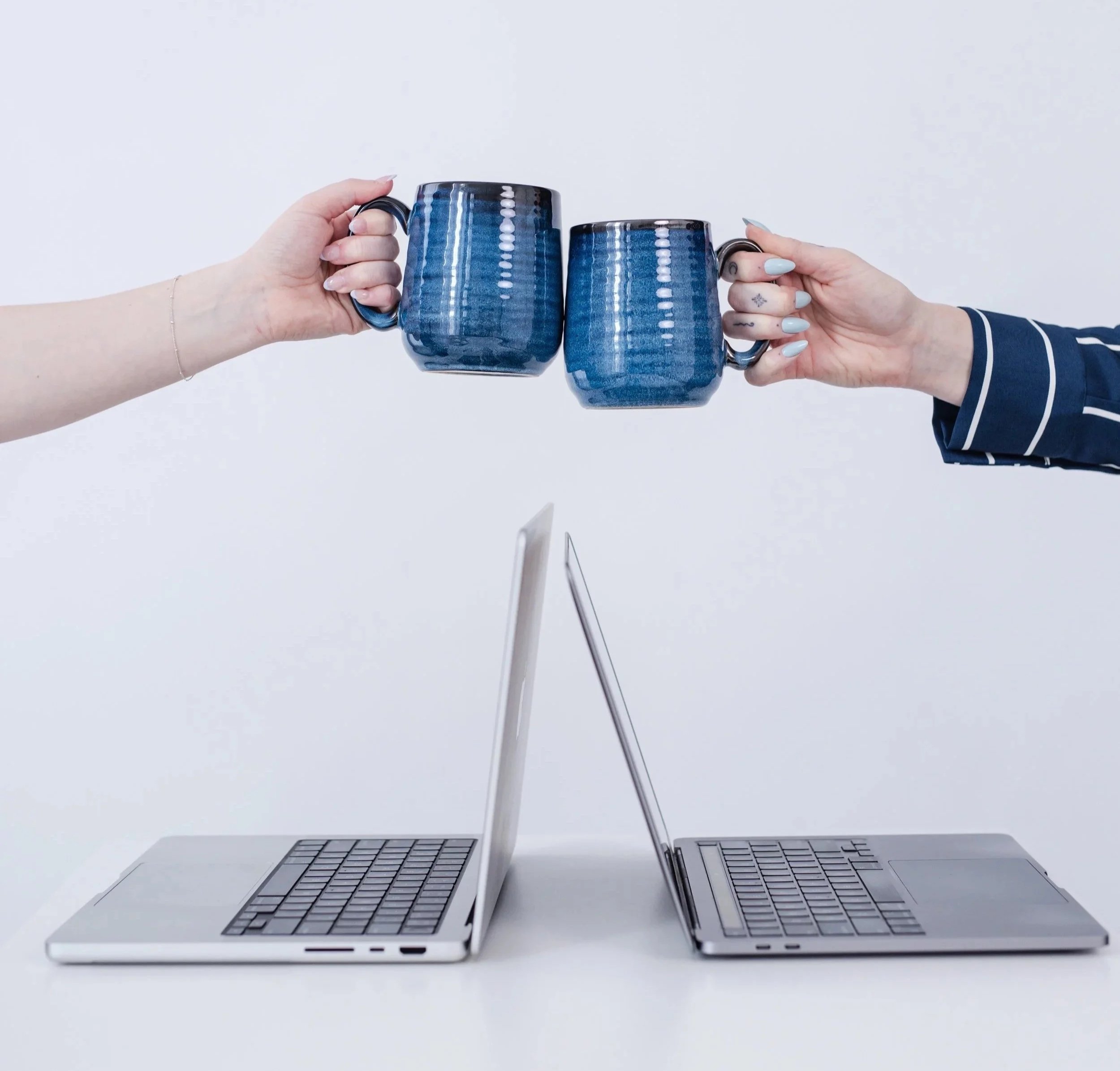 Cheers with coffee mugs over two laptops