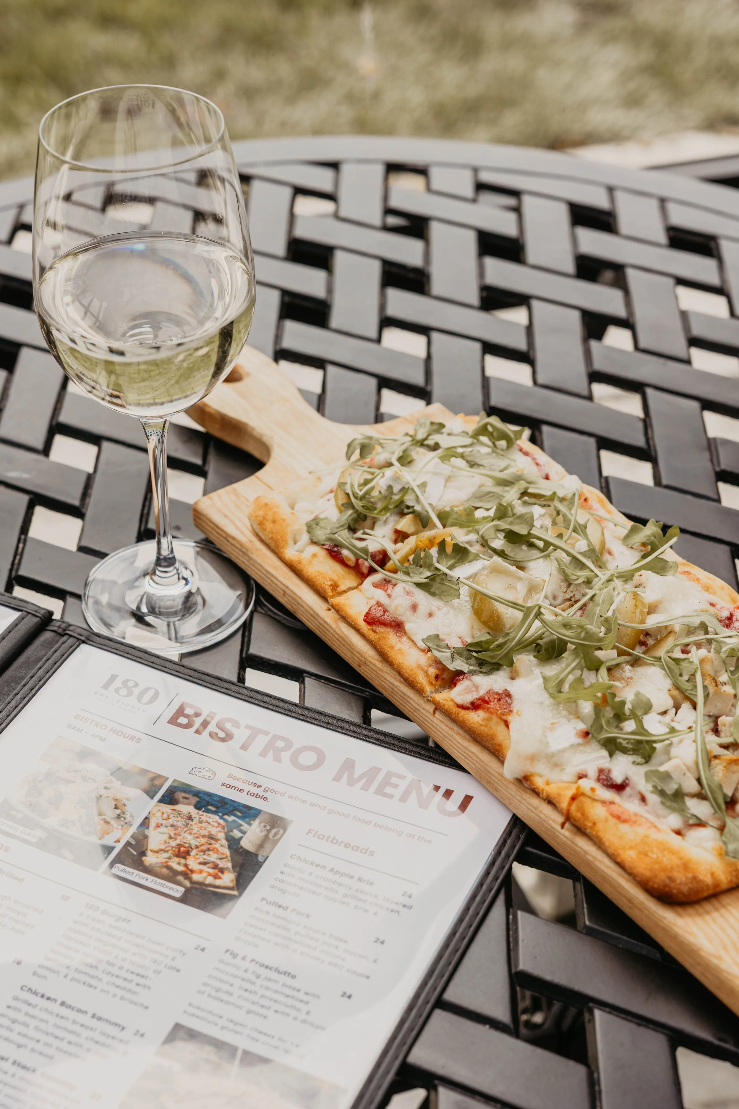 black patio table with a glass of white wine, a board with flatbread and a menu