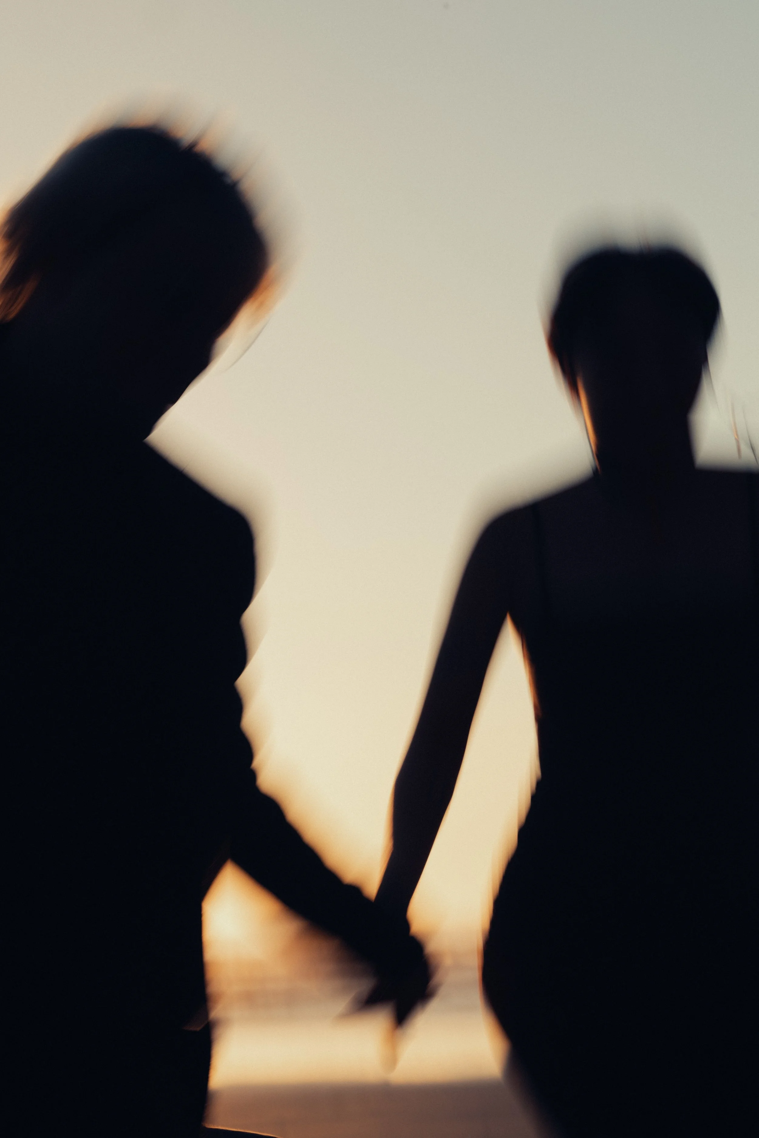 Silhouettes of a man and woman holding hands at sunset on the beach.