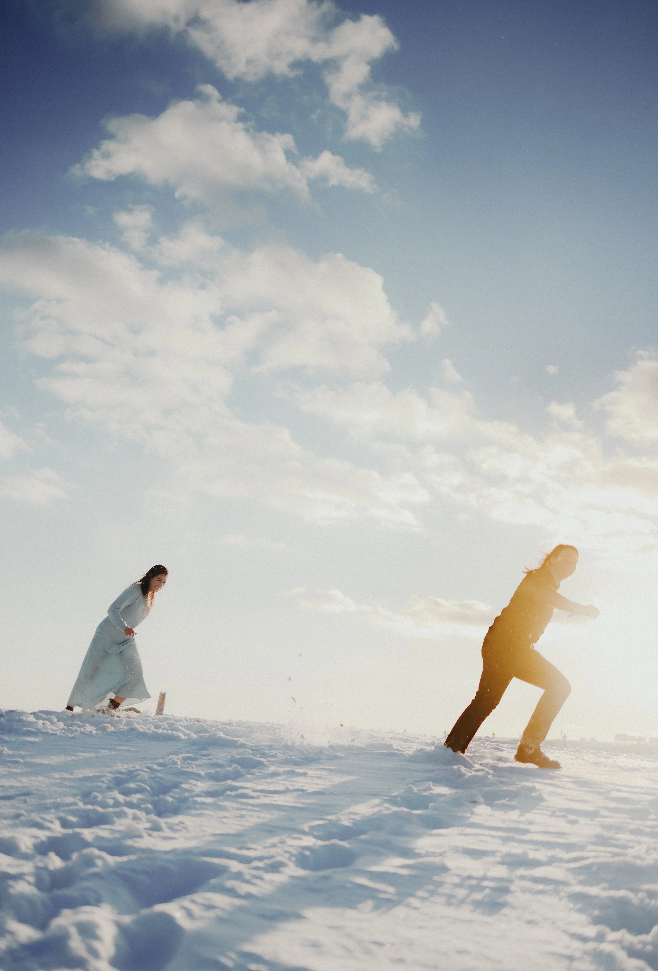 Two women playing in the snow on a sunny day with a partly cloudy sky.