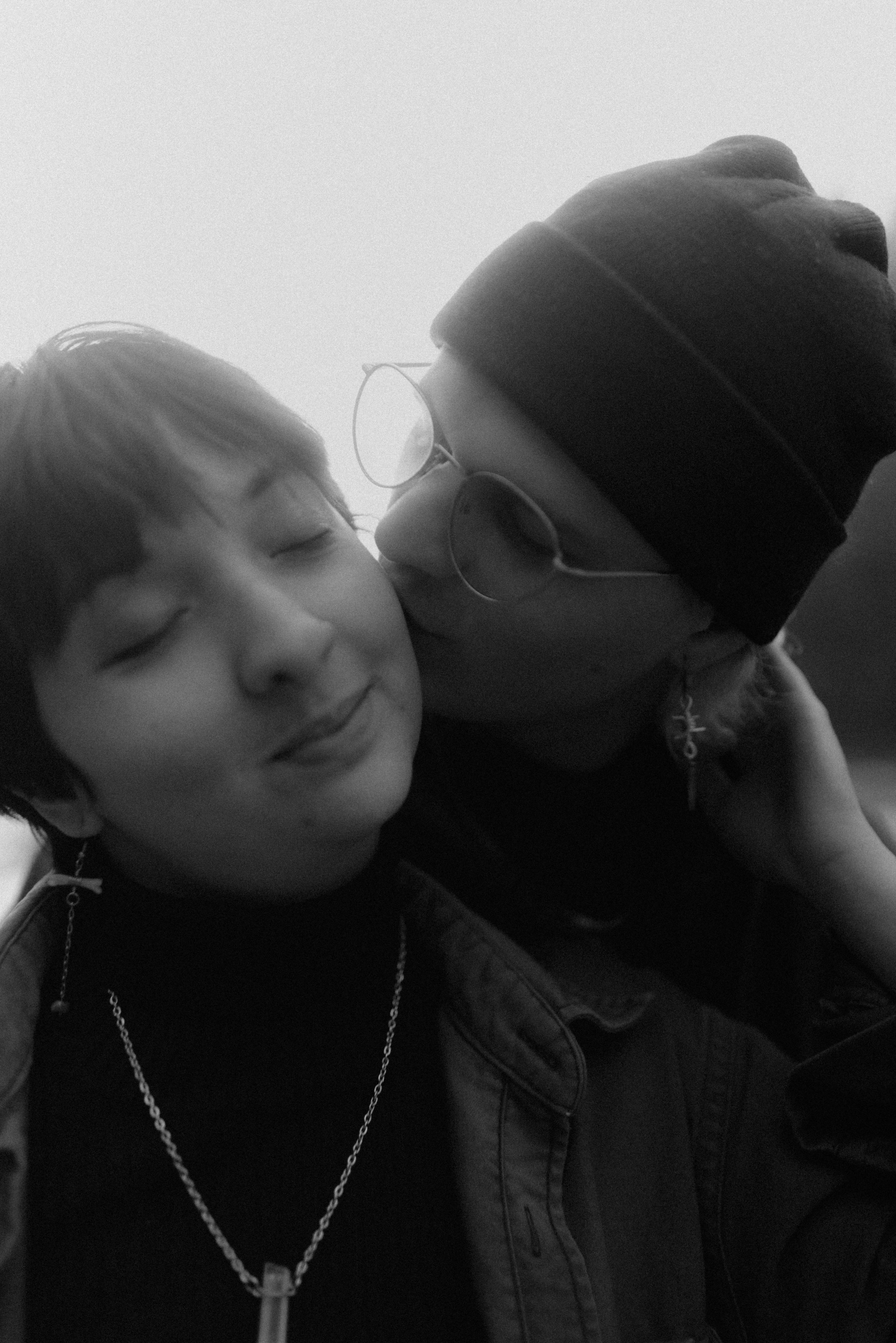 A person wearing glasses and a beanie is kissing a young boy on the cheek; the boy has closed eyes and a slight smile.