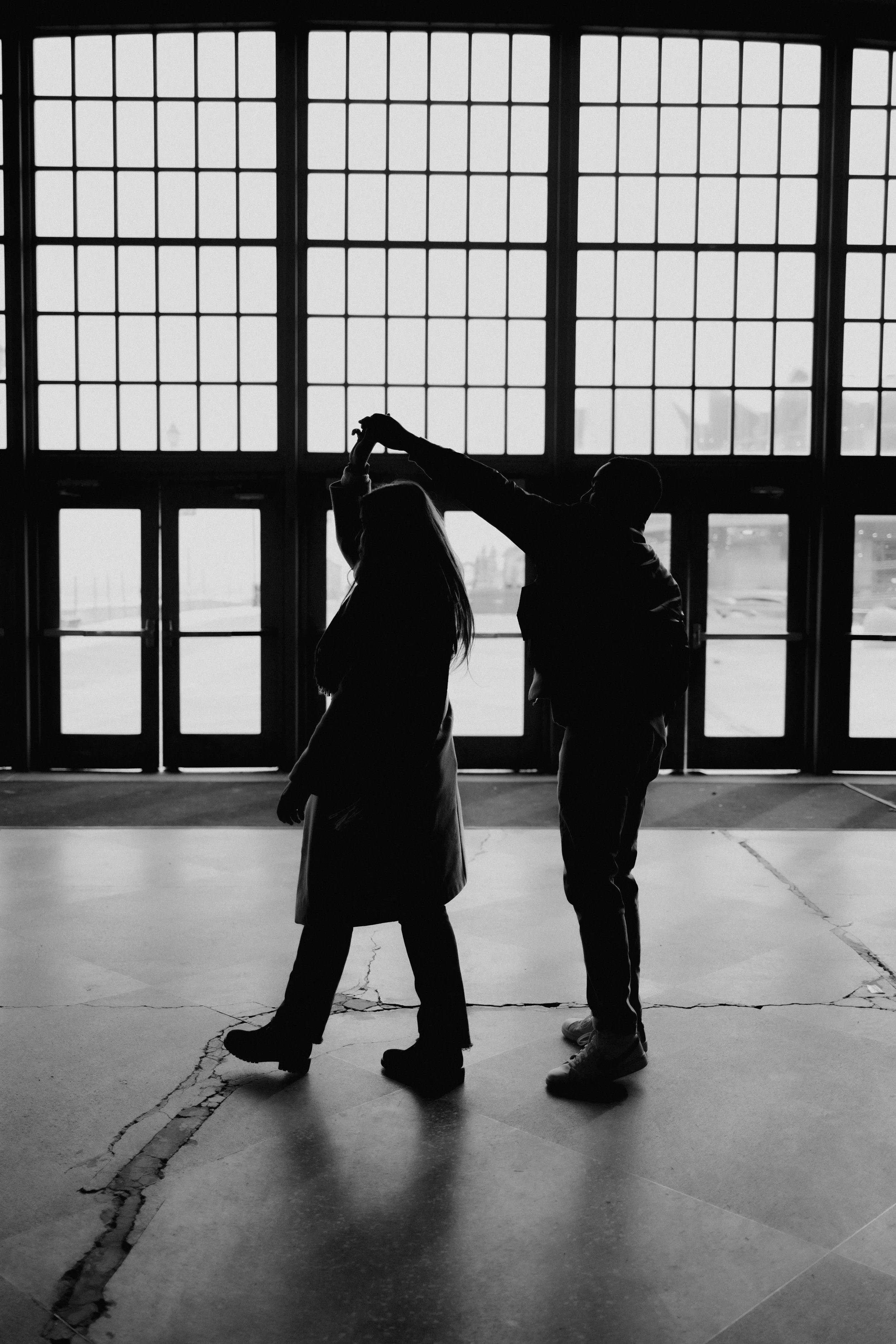Silhouette of a couple dancing inside a building with large grid windows in the background.