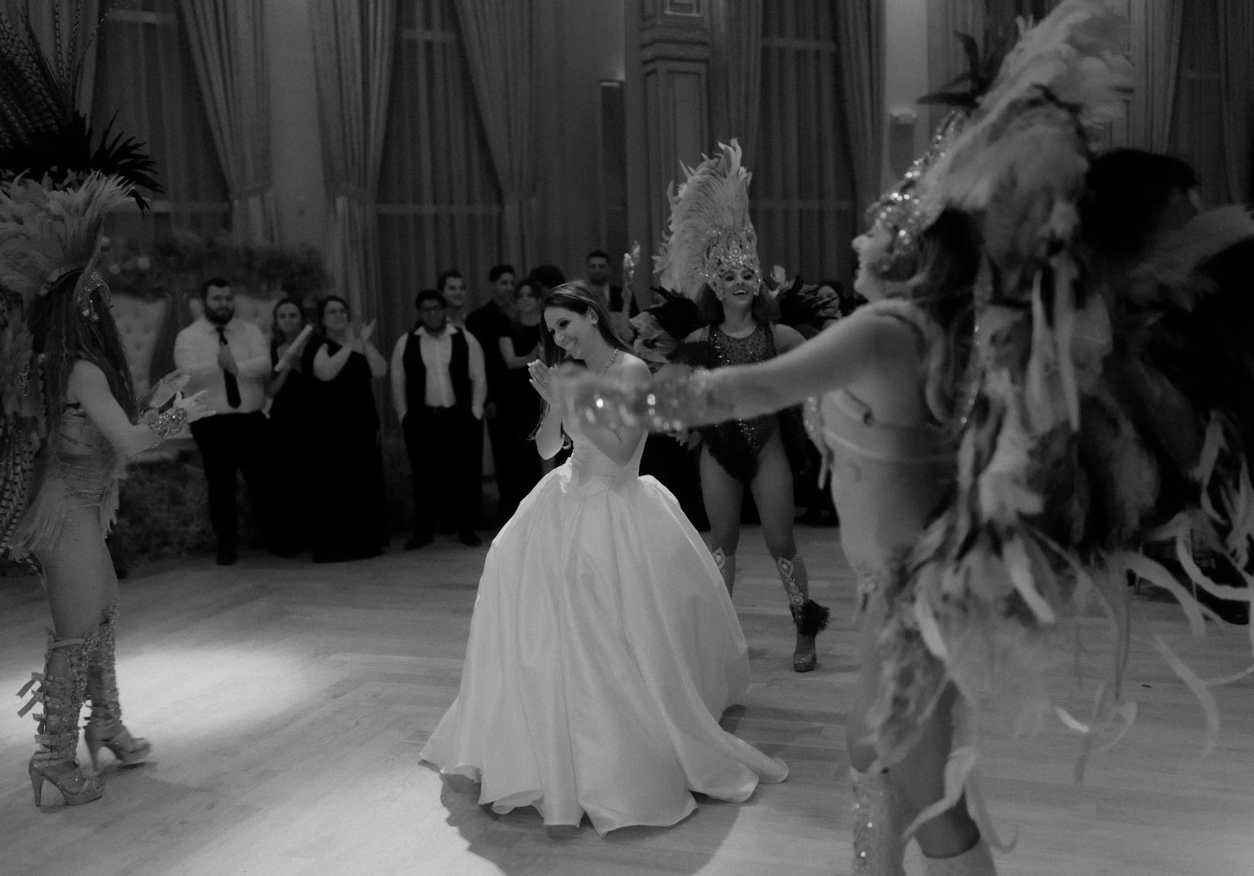 A woman in a white gown dancing with three dancers in carnival costumes with feathered headdresses at a celebration or party.
