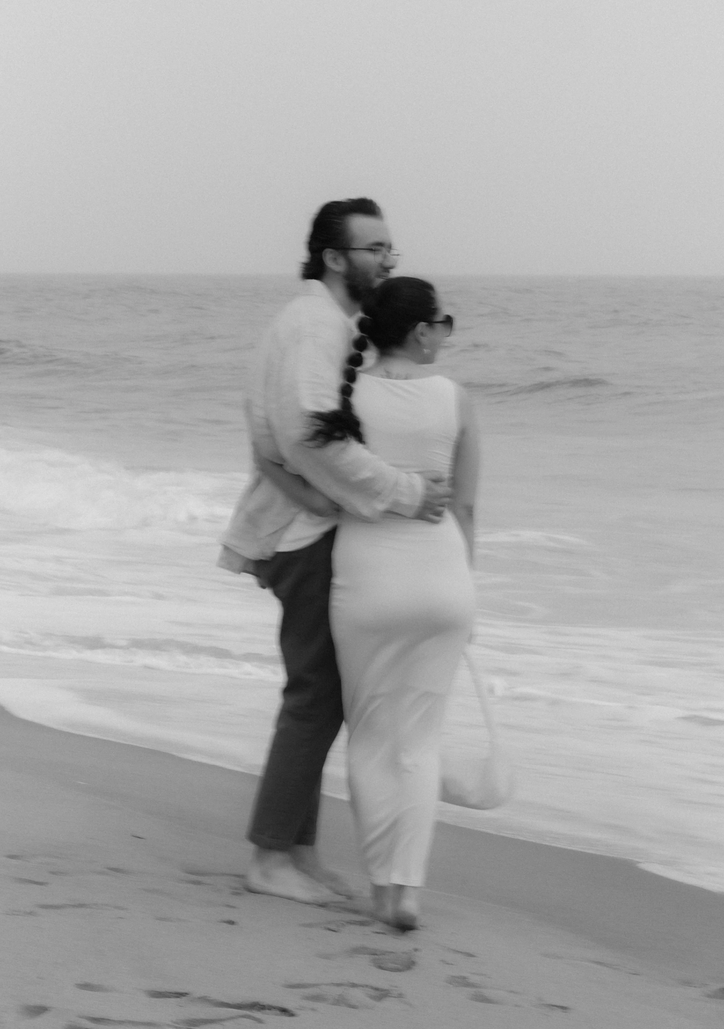 A couple walking along the beach holding each other, with the ocean in the background.