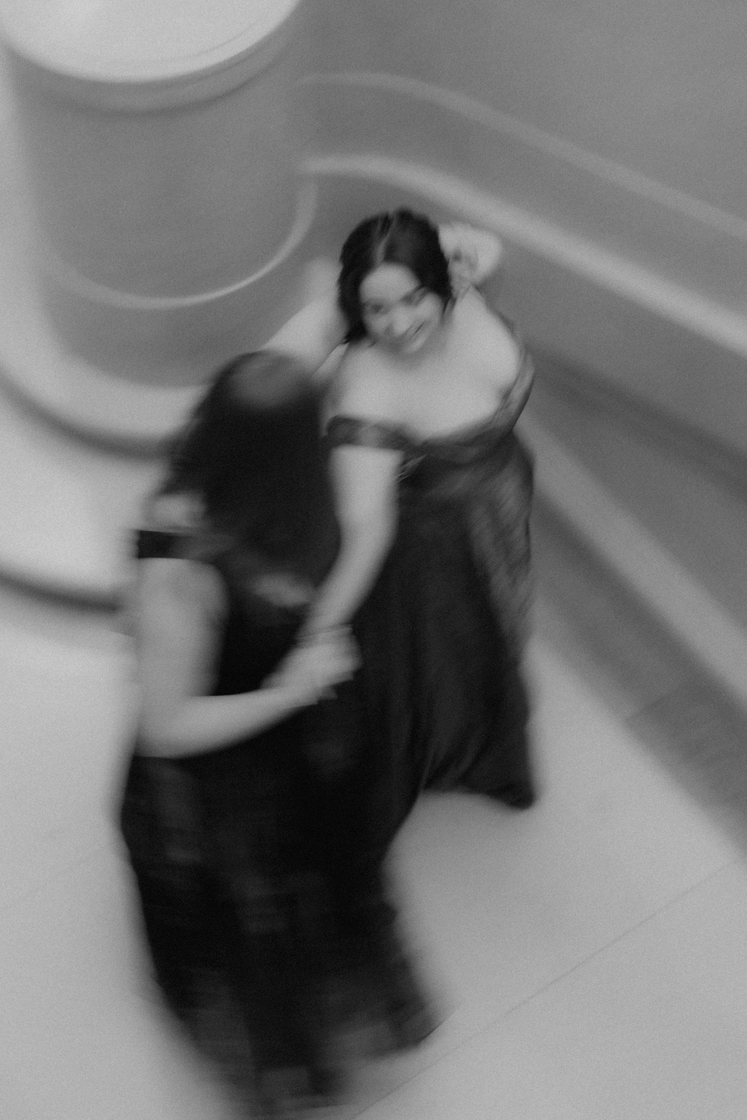Two women in black dresses smiling and holding hands, seen from above in black and white.