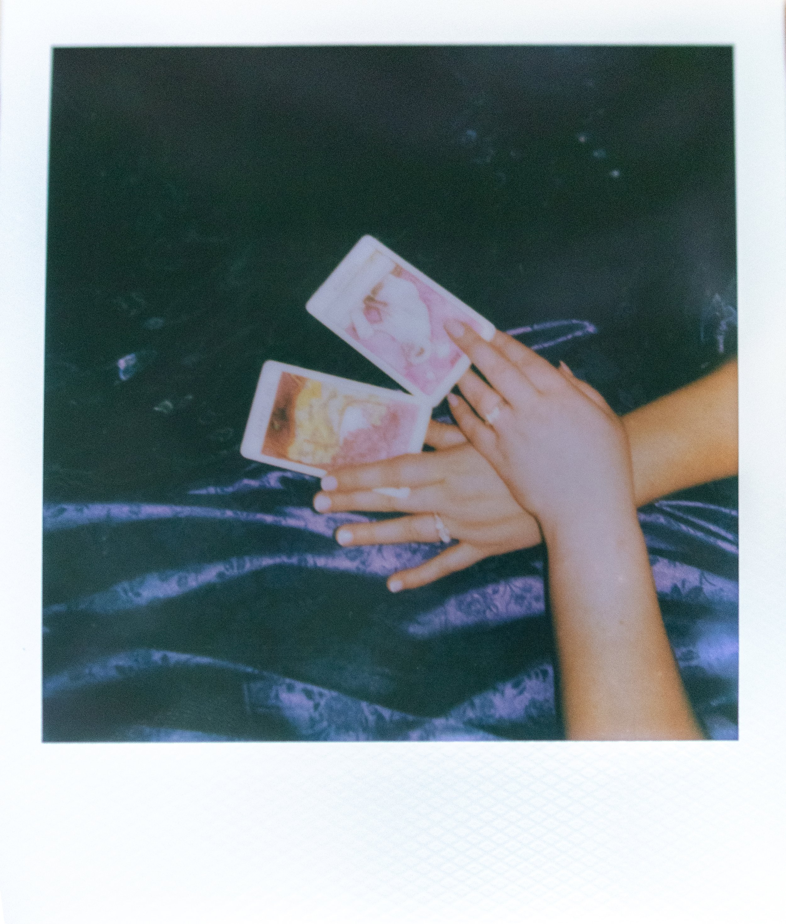 two hands touching and holding tarot cards, showing their engagement rings, on a polaroid photo