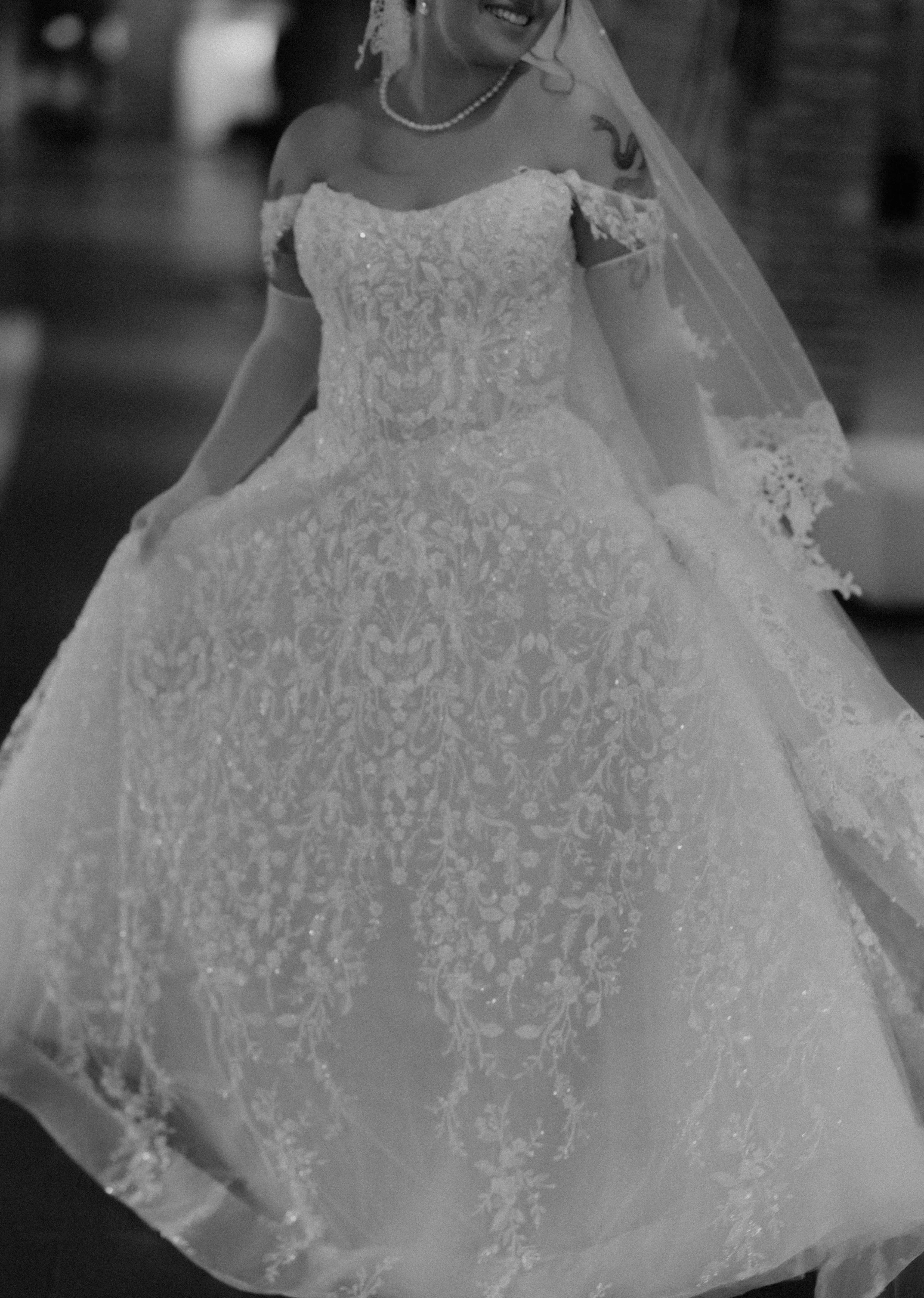 A bride wearing a wedding dress with lace details and a veil, holding the skirt of her dress.