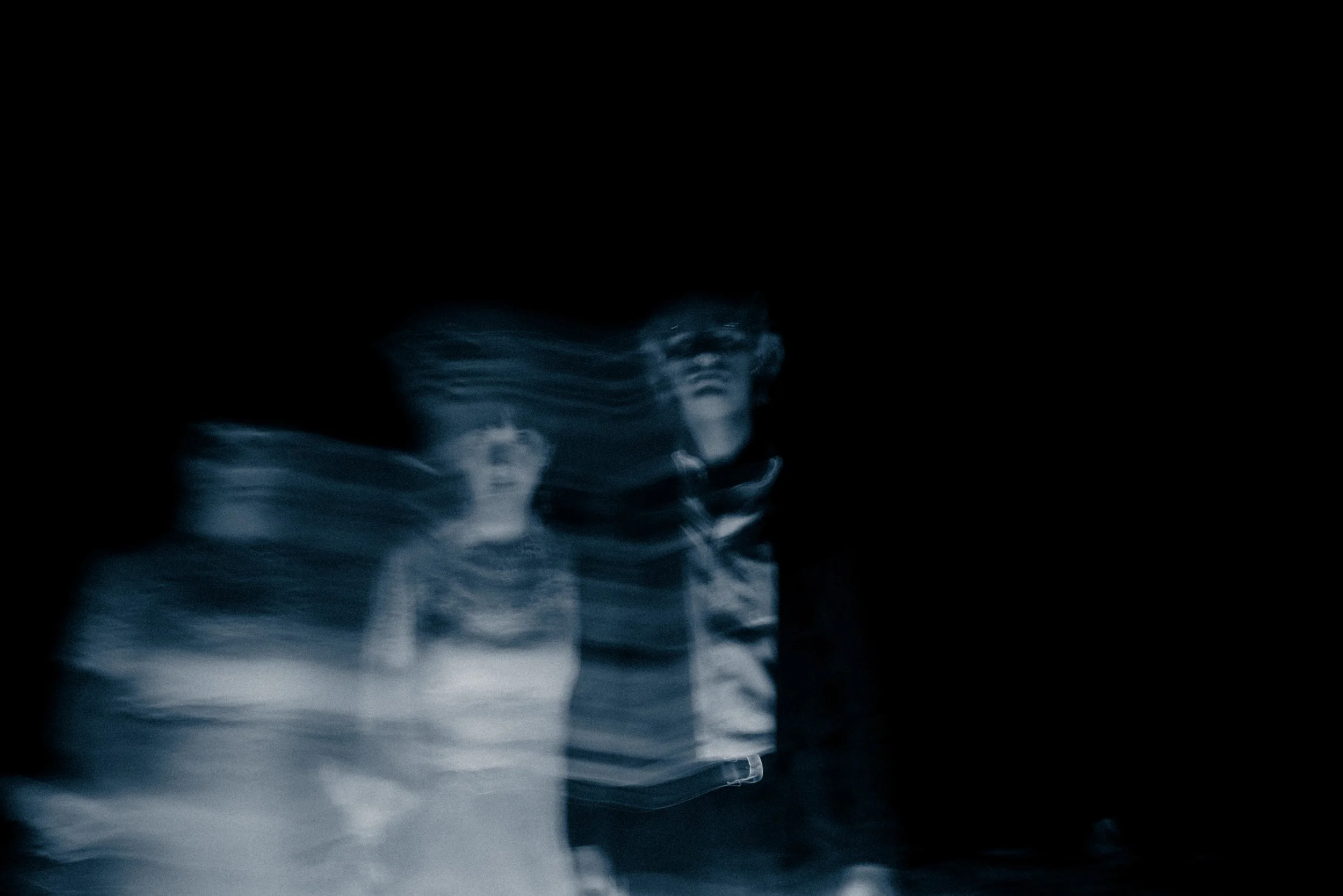 Blurred motion picture of two children in a dark setting, one boy and one girl, with the girl's face more visible, captured with a slow shutter speed.