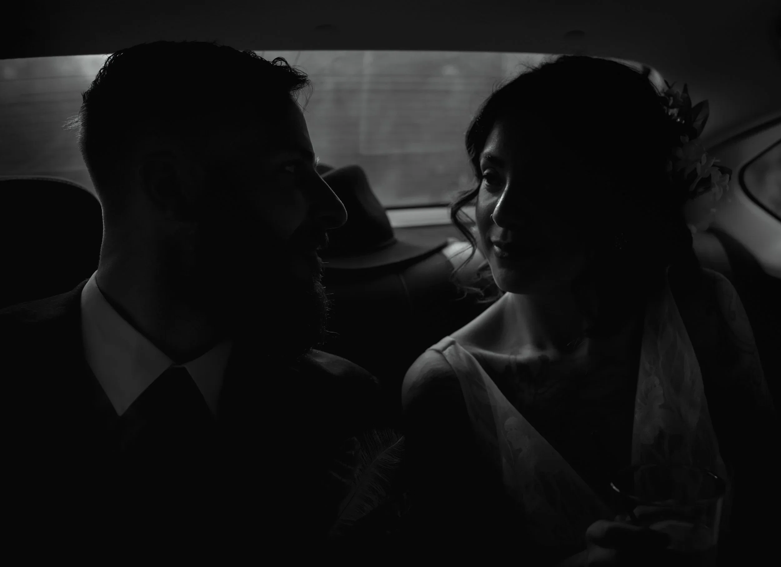 Silhouette of a couple sitting close together in the backseat of a car, sharing a moment during daylight.