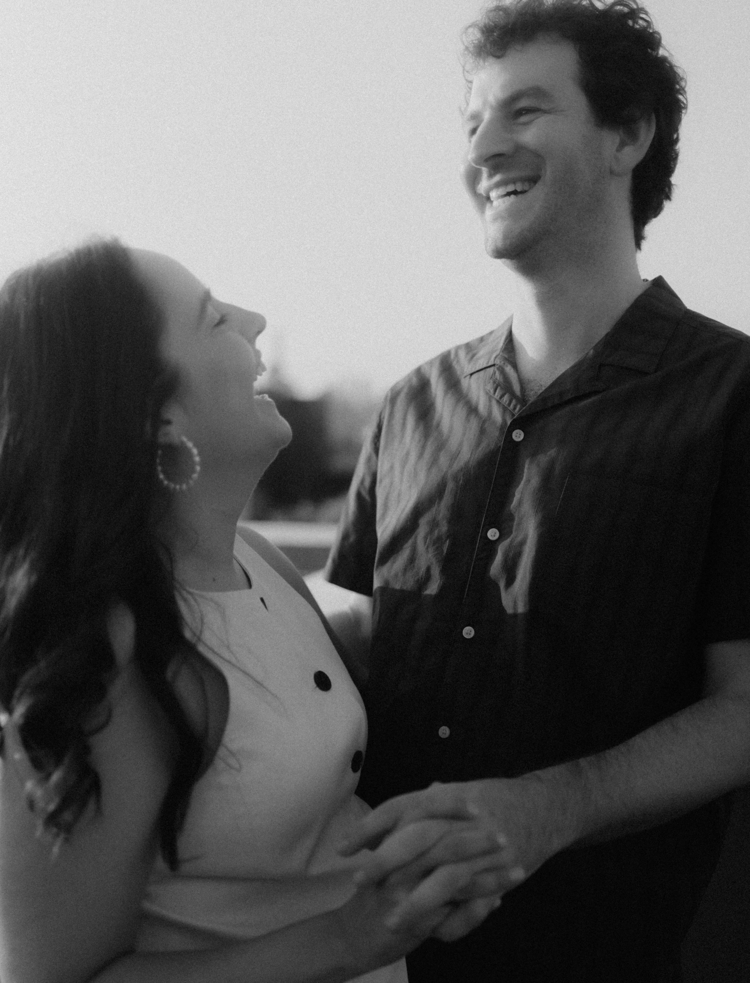 A man and woman smiling at each other while holding hands outside, in black and white.