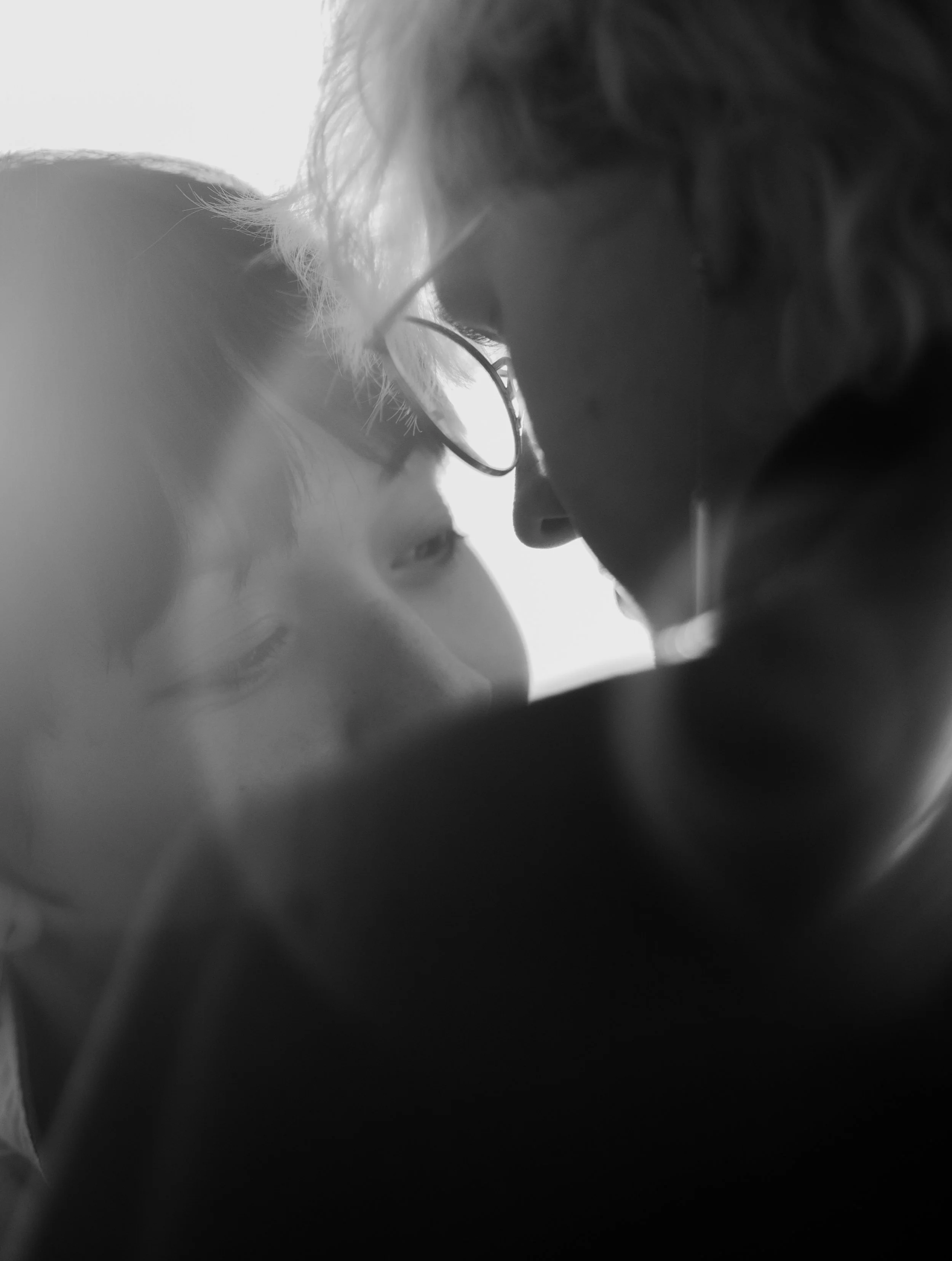 Close-up black and white photo of two people, an adult and a child, touching foreheads with eyes closed, sharing an intimate moment.