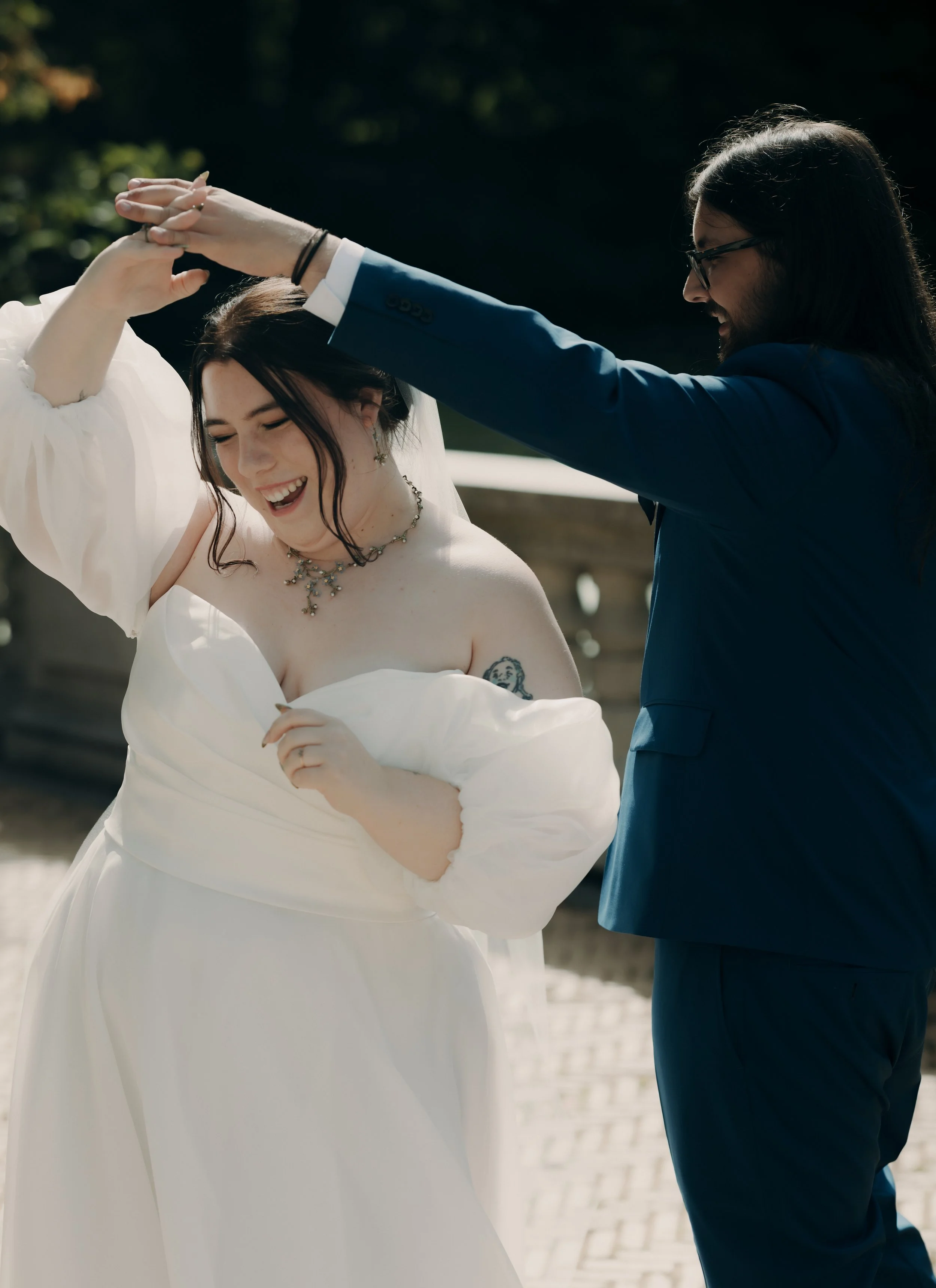 A couple dancing outdoors, smiling, with the woman wearing a white dress and the man in a blue suit.