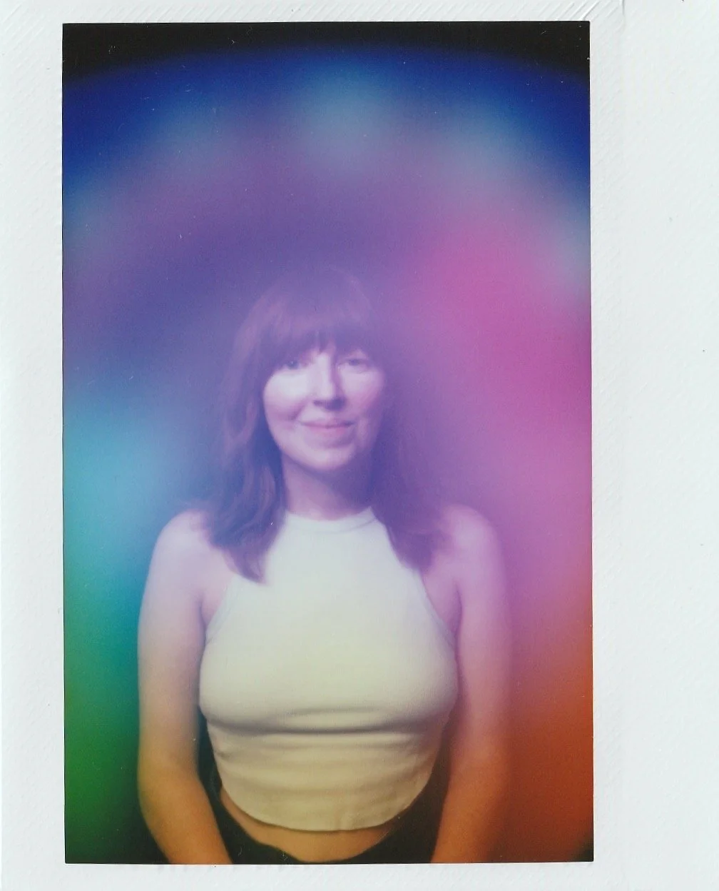 A woman with shoulder-length brown hair and bangs, smiling and wearing a sleeveless cream-colored top.