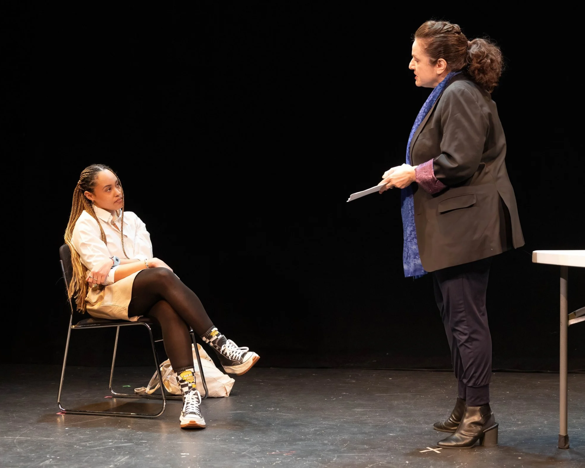 A woman standing and talking to a young girl who is sitting on a chair on a stage with a black background.
