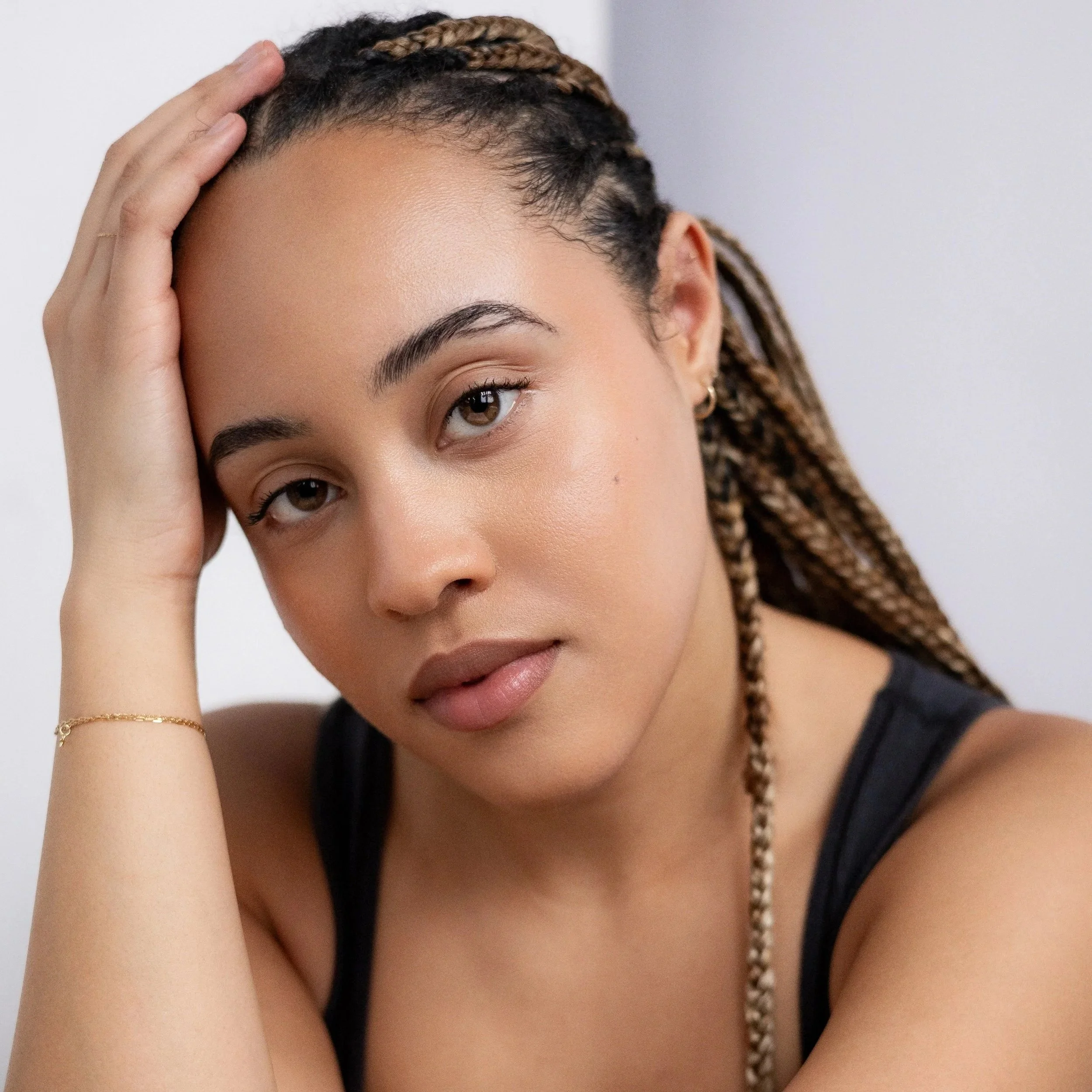 Close-up of a young woman with braided hair, resting her head on her hand, looking calmly at the camera.