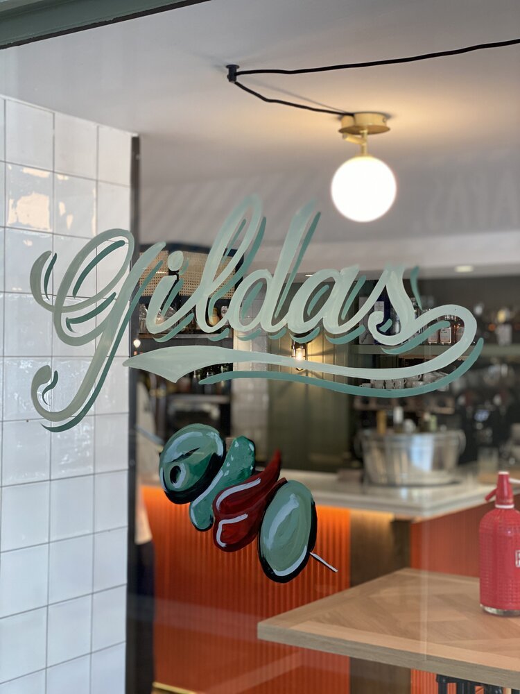 Lettering sobre la ventana de un bar a pincel con esmalte sintético, por Rotulación a mano