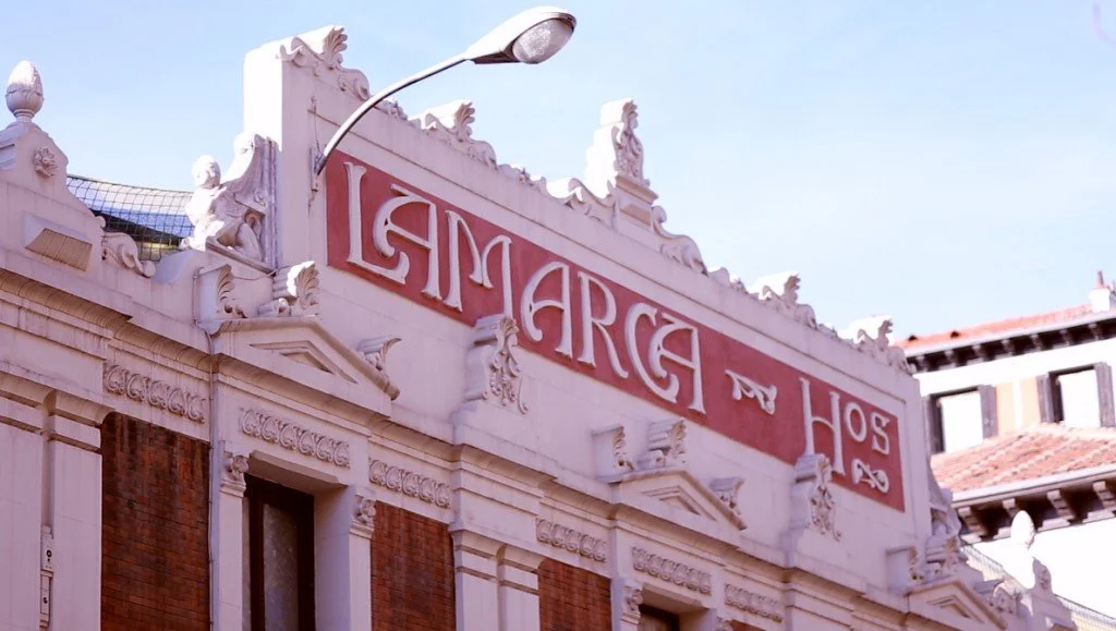 Antigua Fábrica y Taller de Carruajes Lamarca Hermanos, Mezcla estilos Modernistas y clasicistas, como los frontones o algunas decoraciones escultóricas, con otros modernistas como el letrero de la fachada. Una combinación presente también en el edif