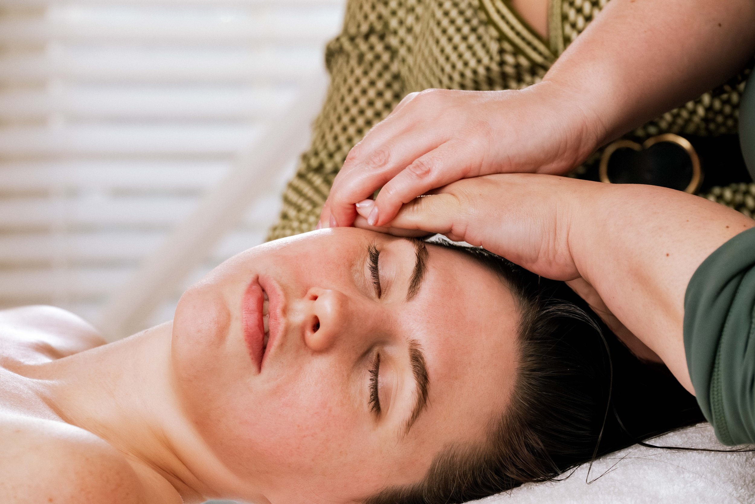 A person receiving an acupressure treatment on their forehead while lying down with eyes closed.